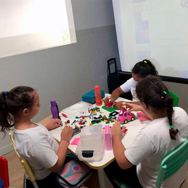 Alunas do fundamental I montando uma construção com blocos de encaixe ao redor de uma mesa