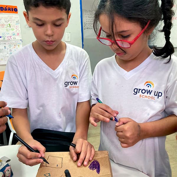 Dupla de alunos do fundamental I desenhando juntos sobre uma caixa de papelão