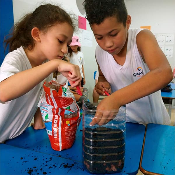 Dupla de alunos do fundamental I montando um terrário em garrafa, em camadas de terra