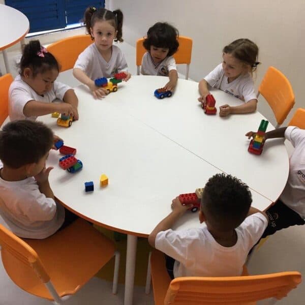 Crianças da educação infantil em volta de uma mesa redonda, montando carrinhos com blocos de encaixe