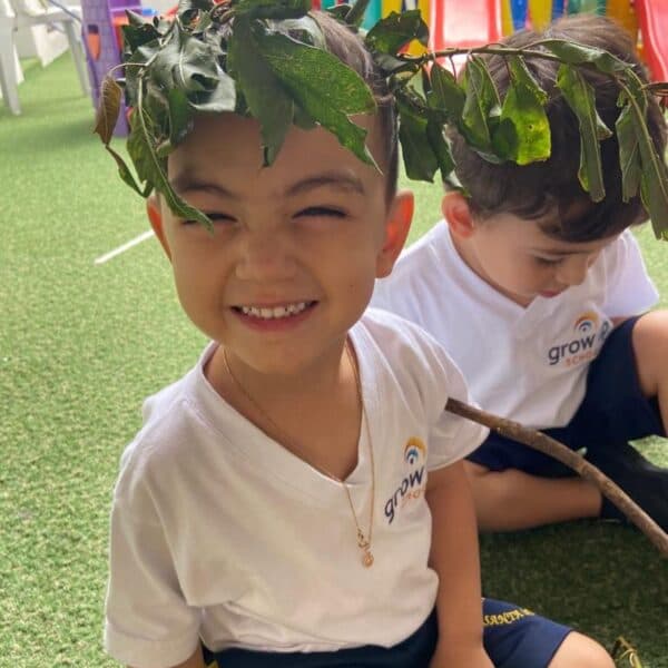 Meninos da educação infantil com coroas de folhas na cabeça, sentados no pátio