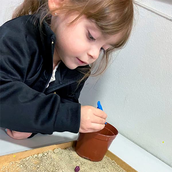 Menina da educação infantil enchendo um vaso com terra usando uma pazinha