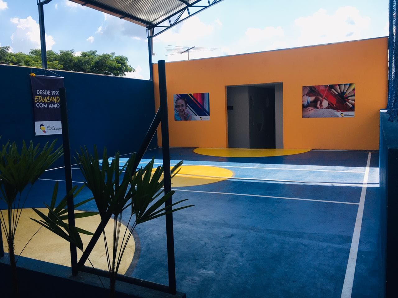 Quadra externa da Grow Up School com piso azul, paredes laranja e área descoberta